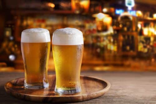 Image de deux pintes de bières posées sur un plateau dans un bar.