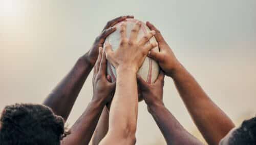 Plusieurs personnes de couleurs différentes touchant un ballon de rugby