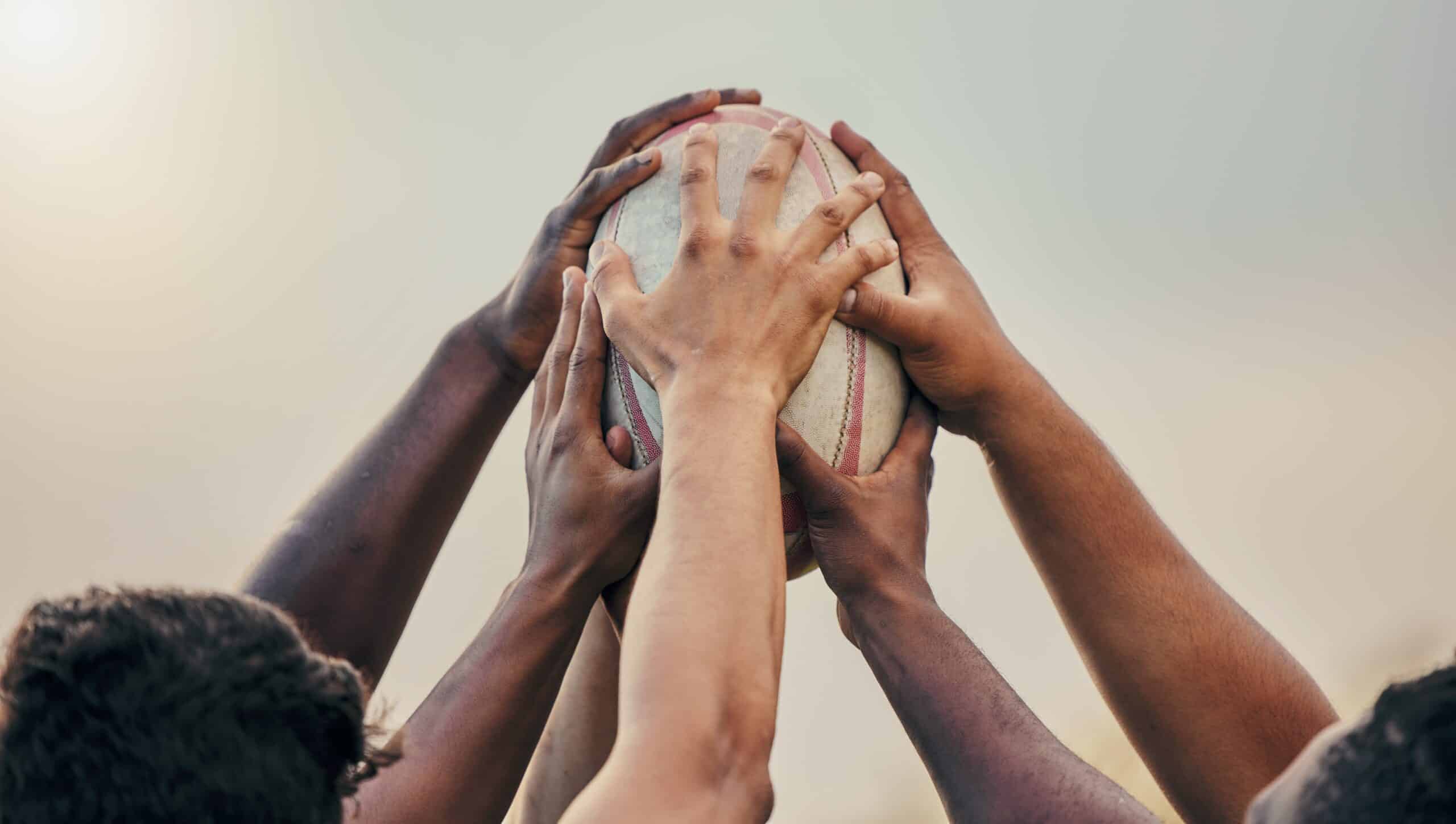 Plusieurs personnes de couleurs différentes touchant un ballon de rugby